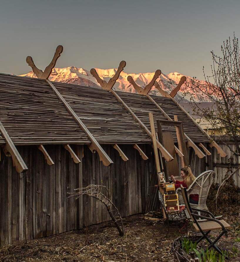 With sunset seeping up the slopes of Mount Timpanogos, Elspeth paints the chickadee on the frame whi...